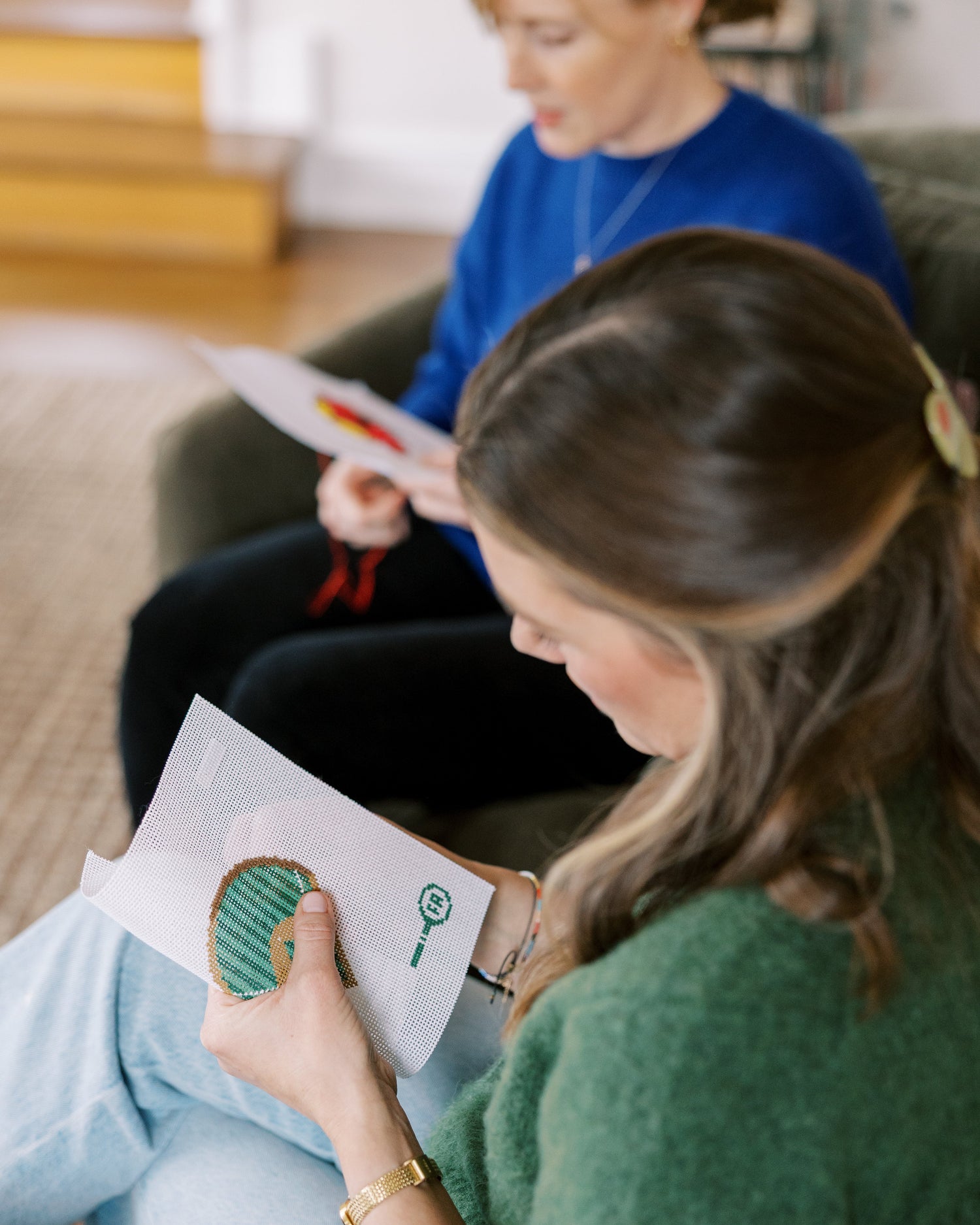 Two women needlepointing siting on chairs next to each other with their own crafts.