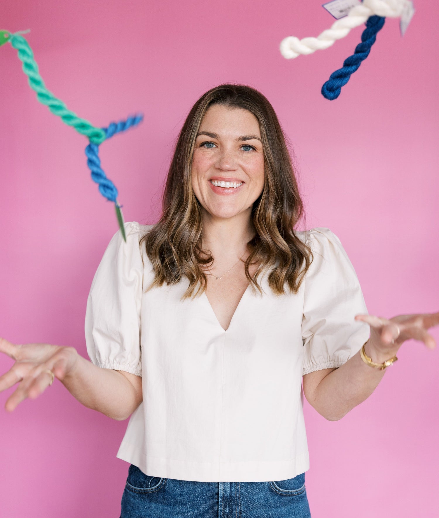 Needlepoint Threads Explained by Becca throwing thread in front of a pink background.