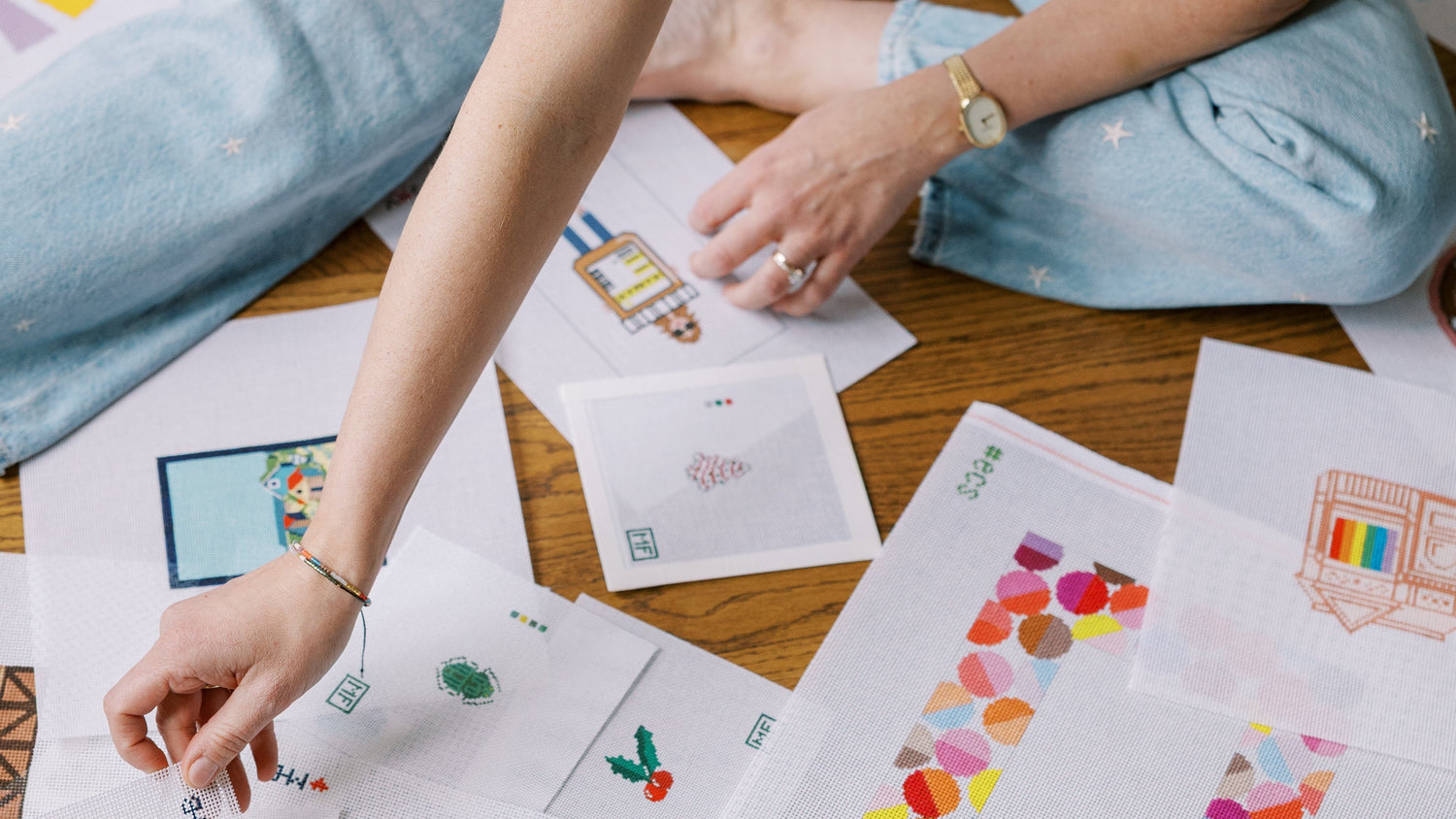 Rebecca sitting on the floor with colorful needlepoint canvases spread out around her