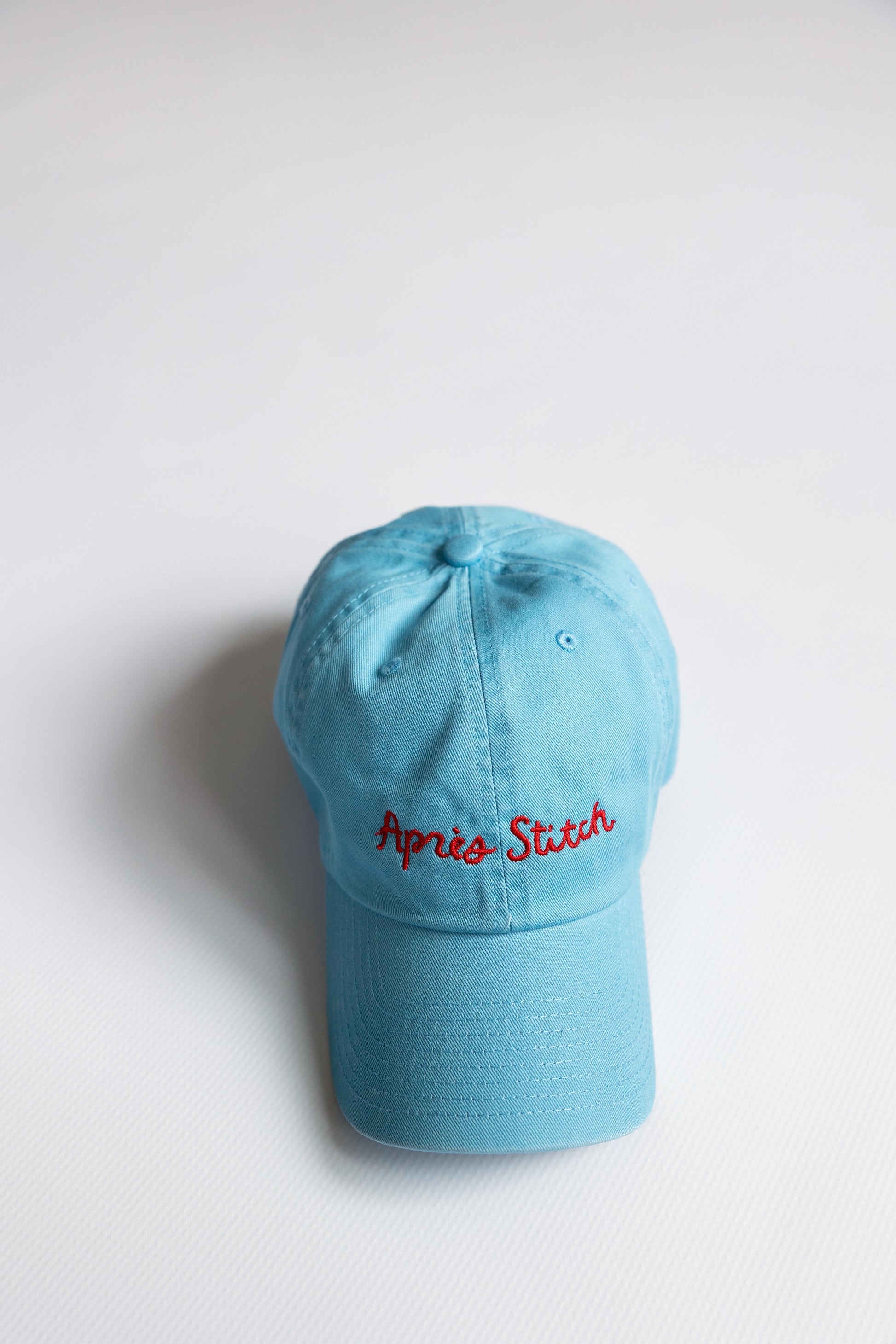 Light blue cap with 'Apres Stitch' text on a white background
