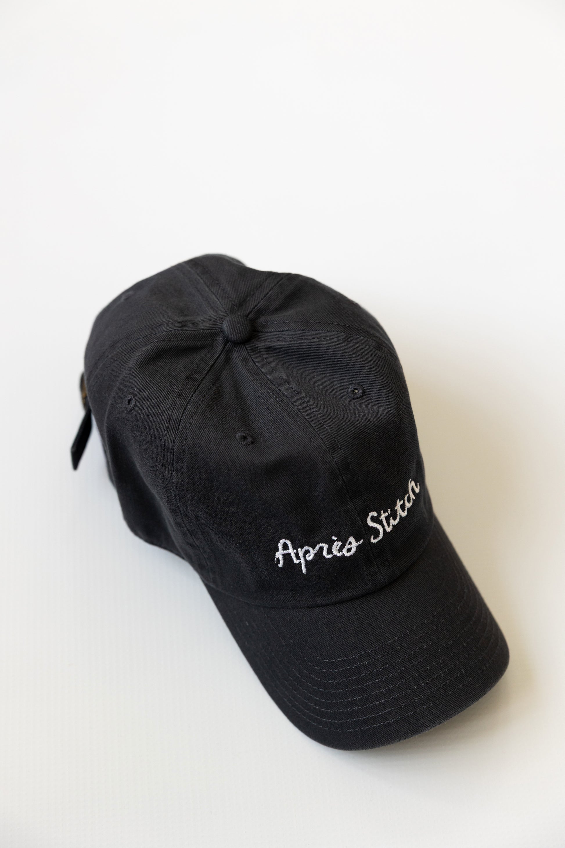 Navy cap with 'Apres Stitch' white embroidery on a white background