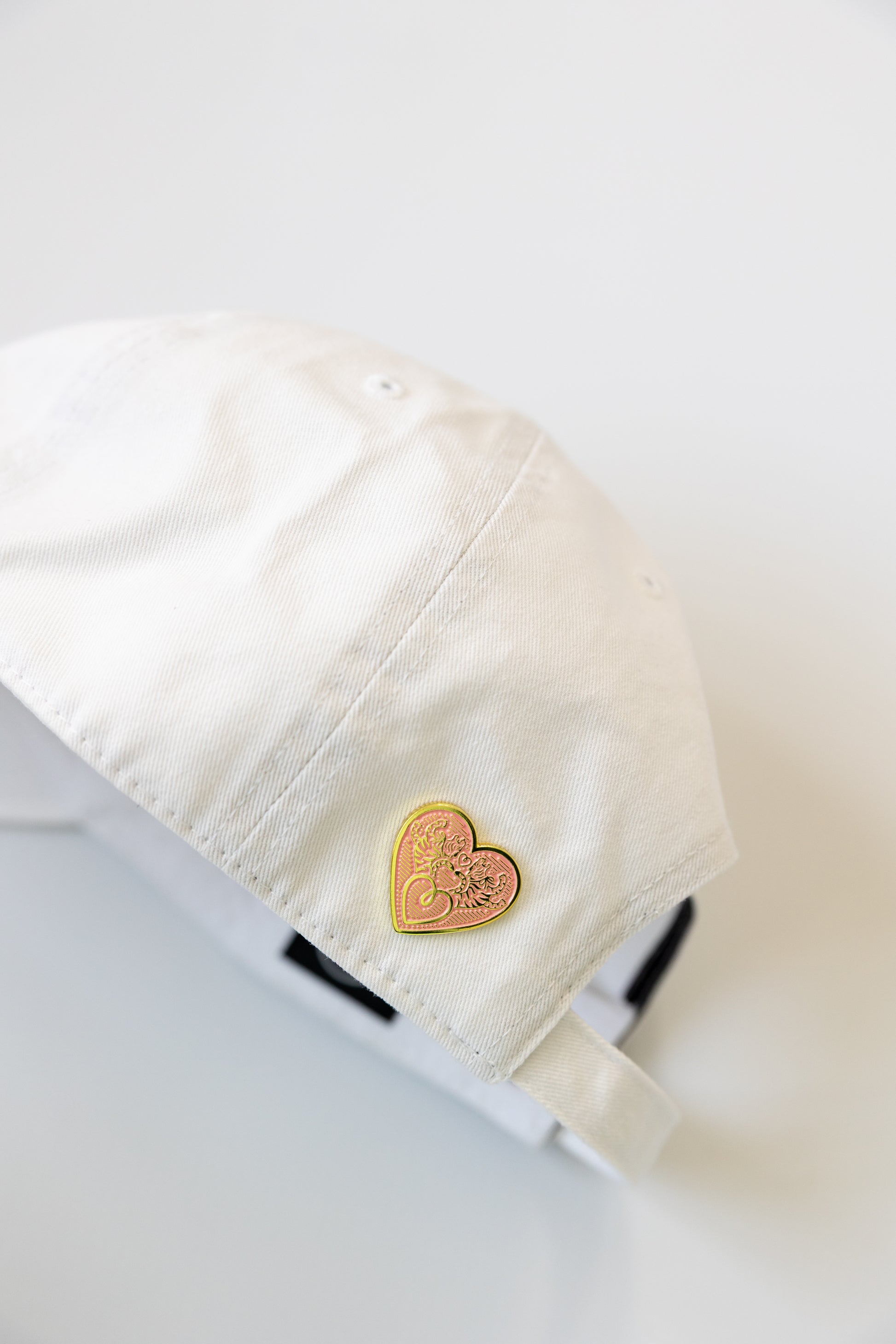 Heart-shaped gold pin on a white hat against a white background