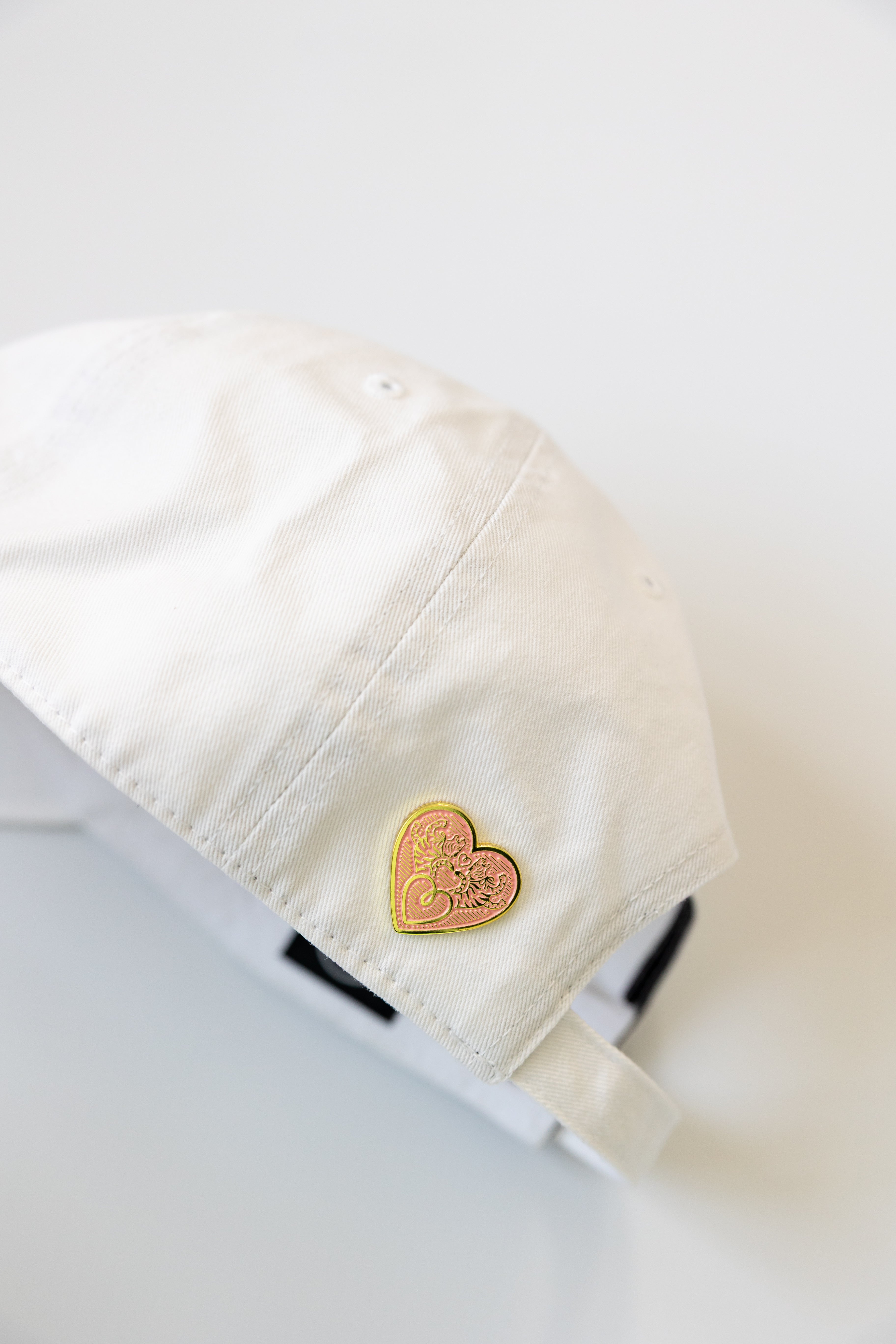 Heart-shaped gold pin on a white hat against a white background