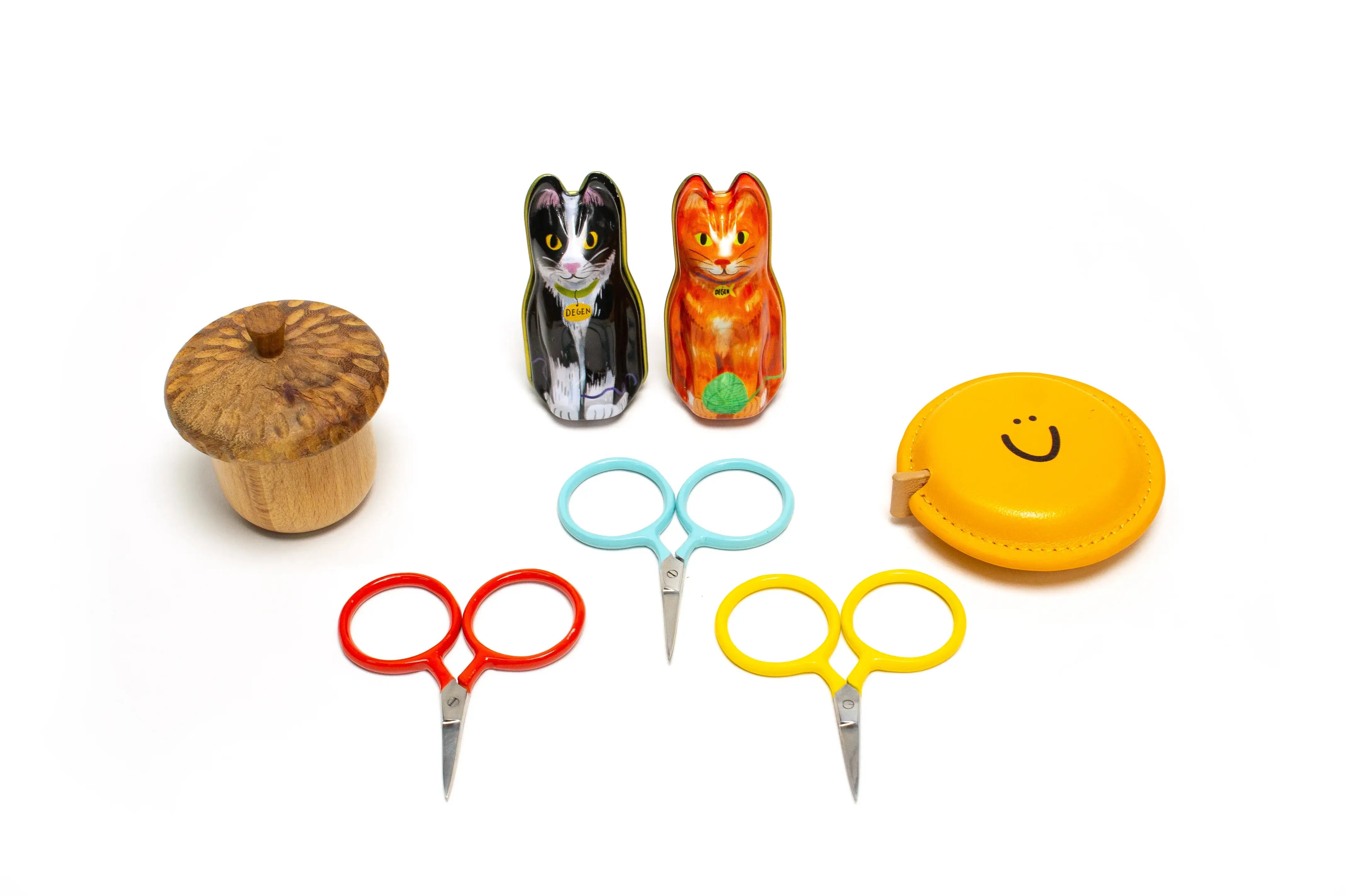 Set of colorful scissors, a wooden spool, and cat-shaped salt and pepper shakers on a white background