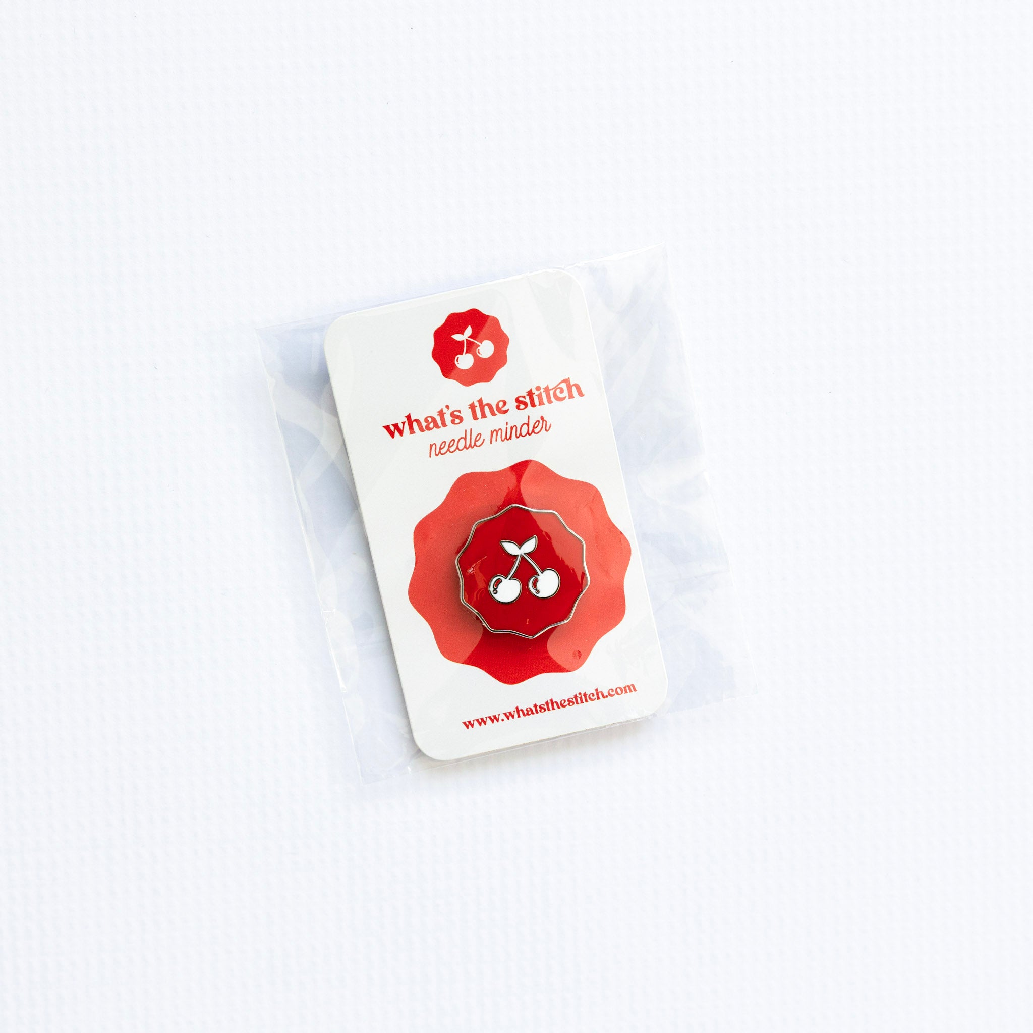 Red and white needle minder with 'What's the Stitch' cherry branding on a white background