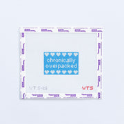 Needlepoint pattern with 'chronically overpacked' text and heart symbols on a white background