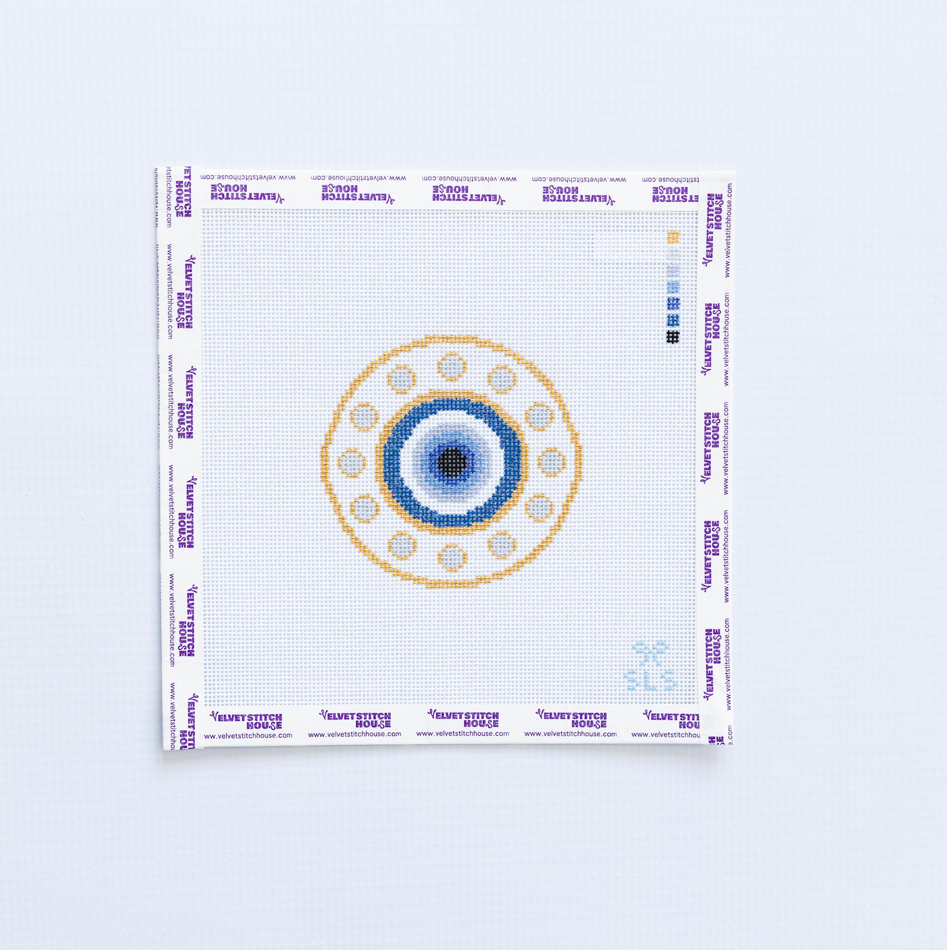 Needlepoint pattern of a blue and gold evil eye with a blue and gold circular design on a white fabric background