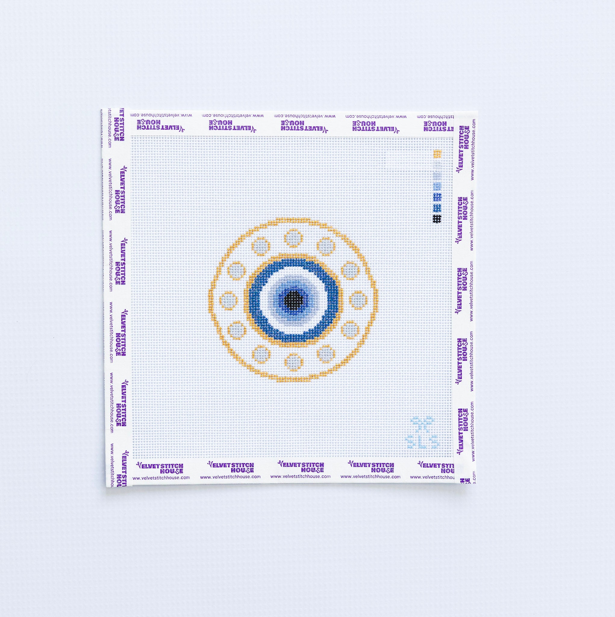 Needlepoint pattern of a blue and gold evil eye with a blue and gold circular design on a white fabric background
