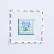 Needlepoint pattern with a blue hydrangea flower on a white fabric with light blue grid pattern