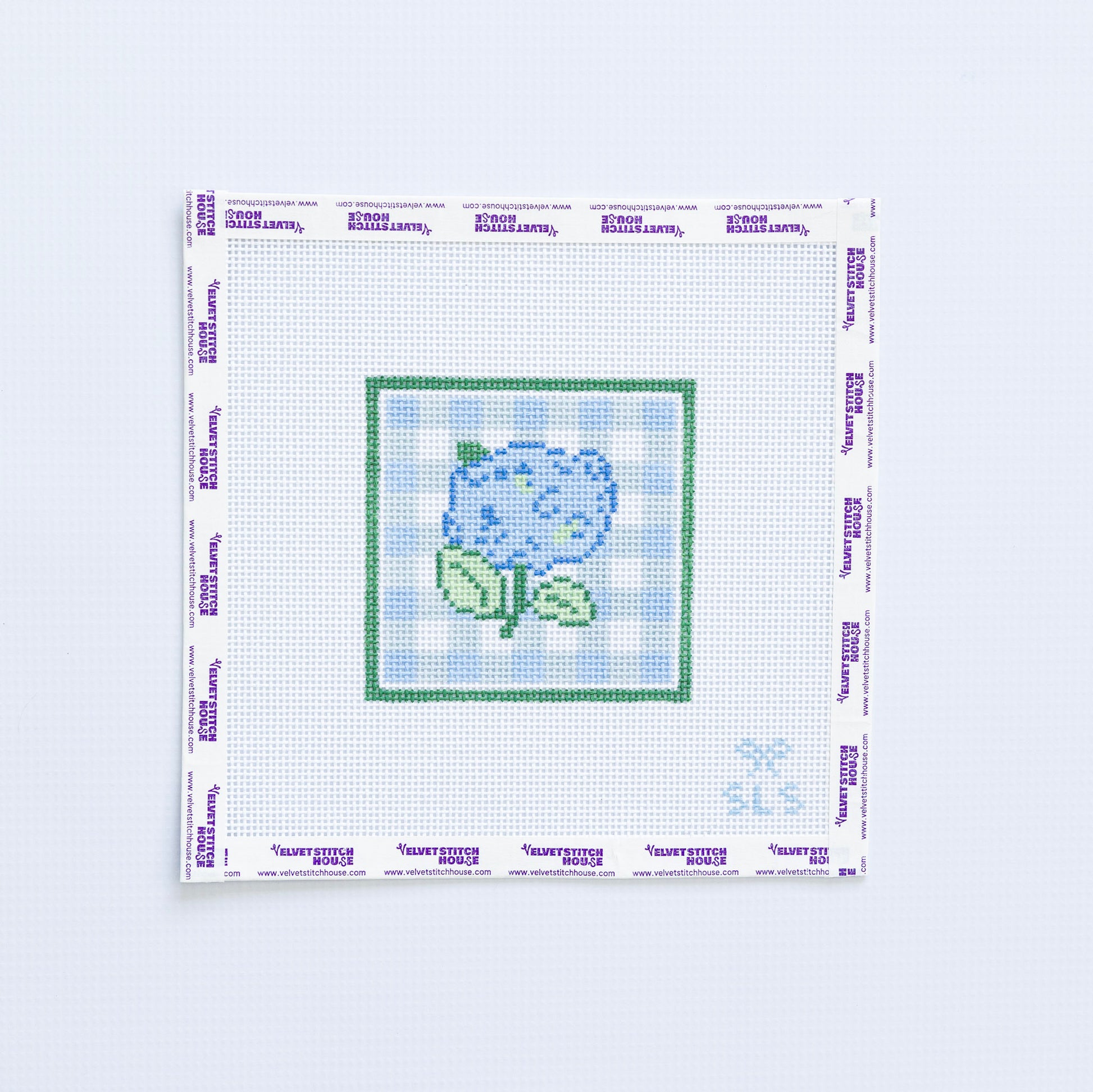 Needlepoint pattern with a blue hydrangea flower on a white fabric with light blue grid pattern