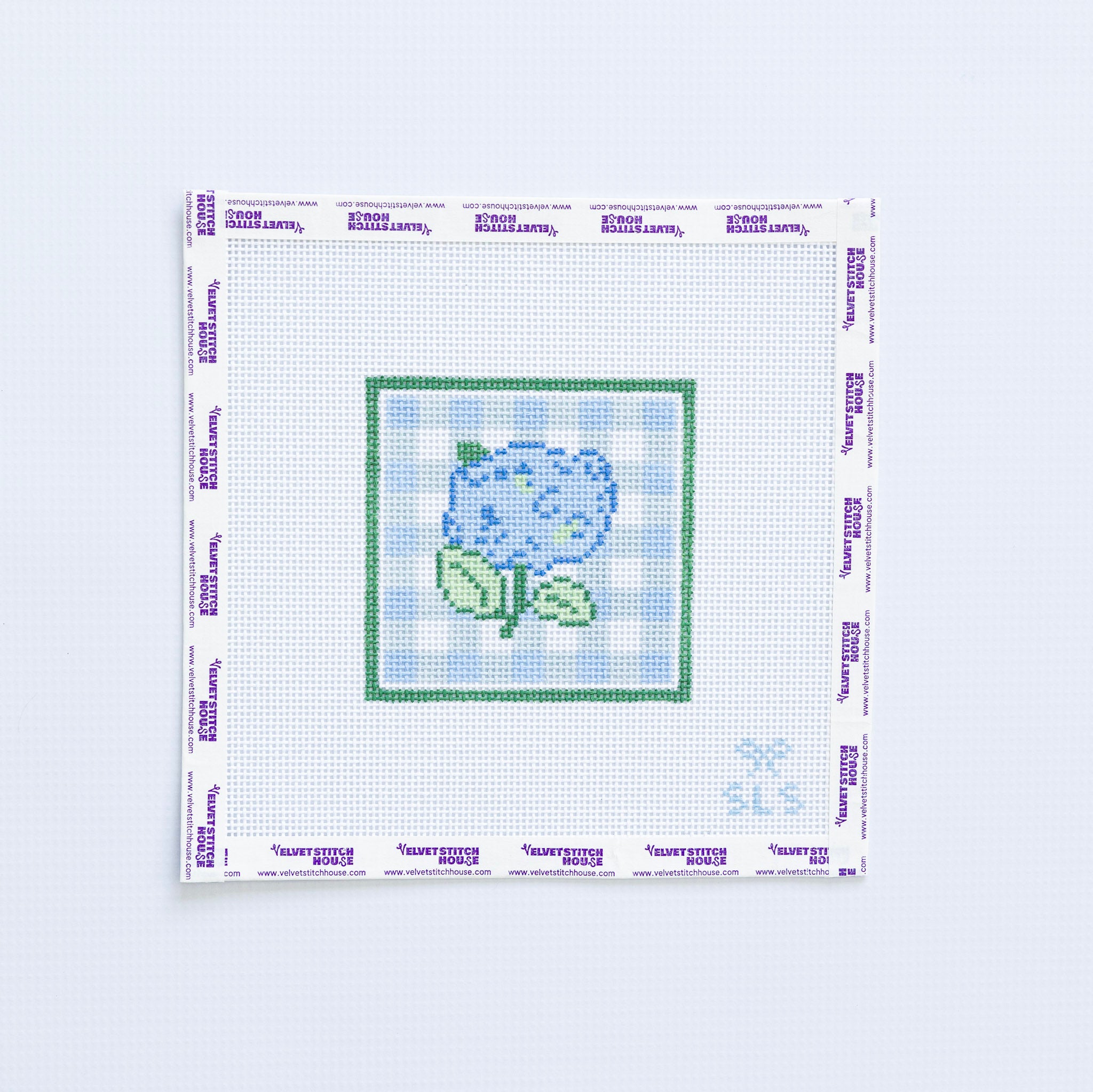 Needlepoint pattern with a blue hydrangea flower on a white fabric with light blue grid pattern