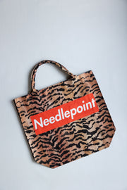 Tote bag with tiger pattern and 'Needlepoint' logo on a red background