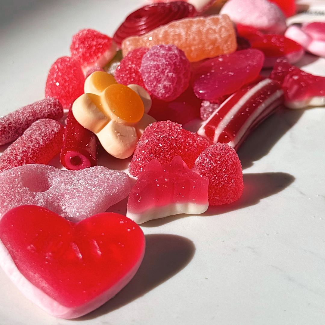 Assorted colorful candies including heart-shaped gummies and licorice on a light background