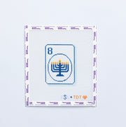 Needlepoint pattern with a menorah design in blue on a mahjong tile on a white background