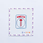 Needlepoint design with 'NORTH' in red and a candy cane pole on a mahjong tile on a white background