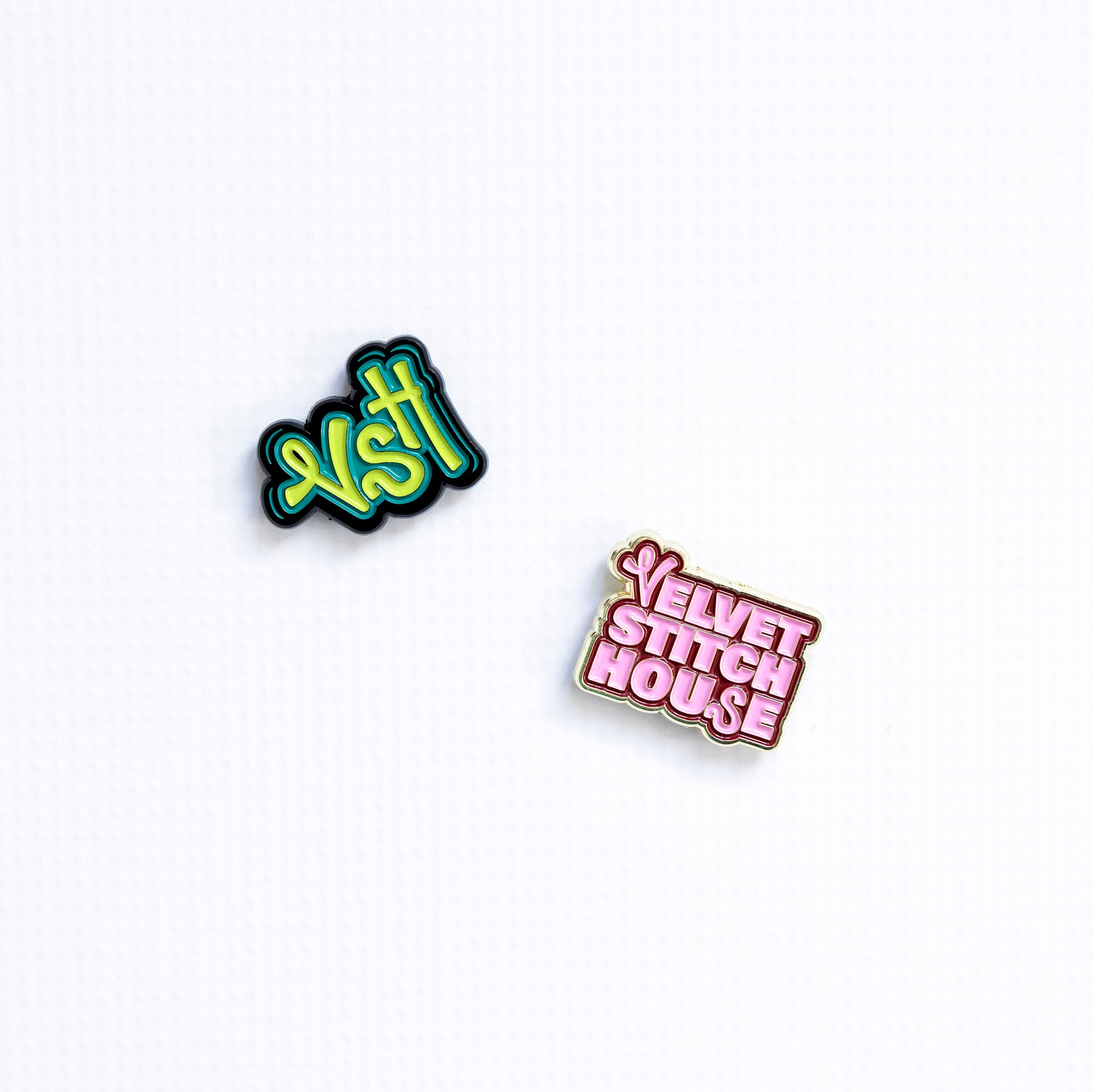 Two enamel pins with 'VSH' and 'Velvet Stitch House' text on a white background