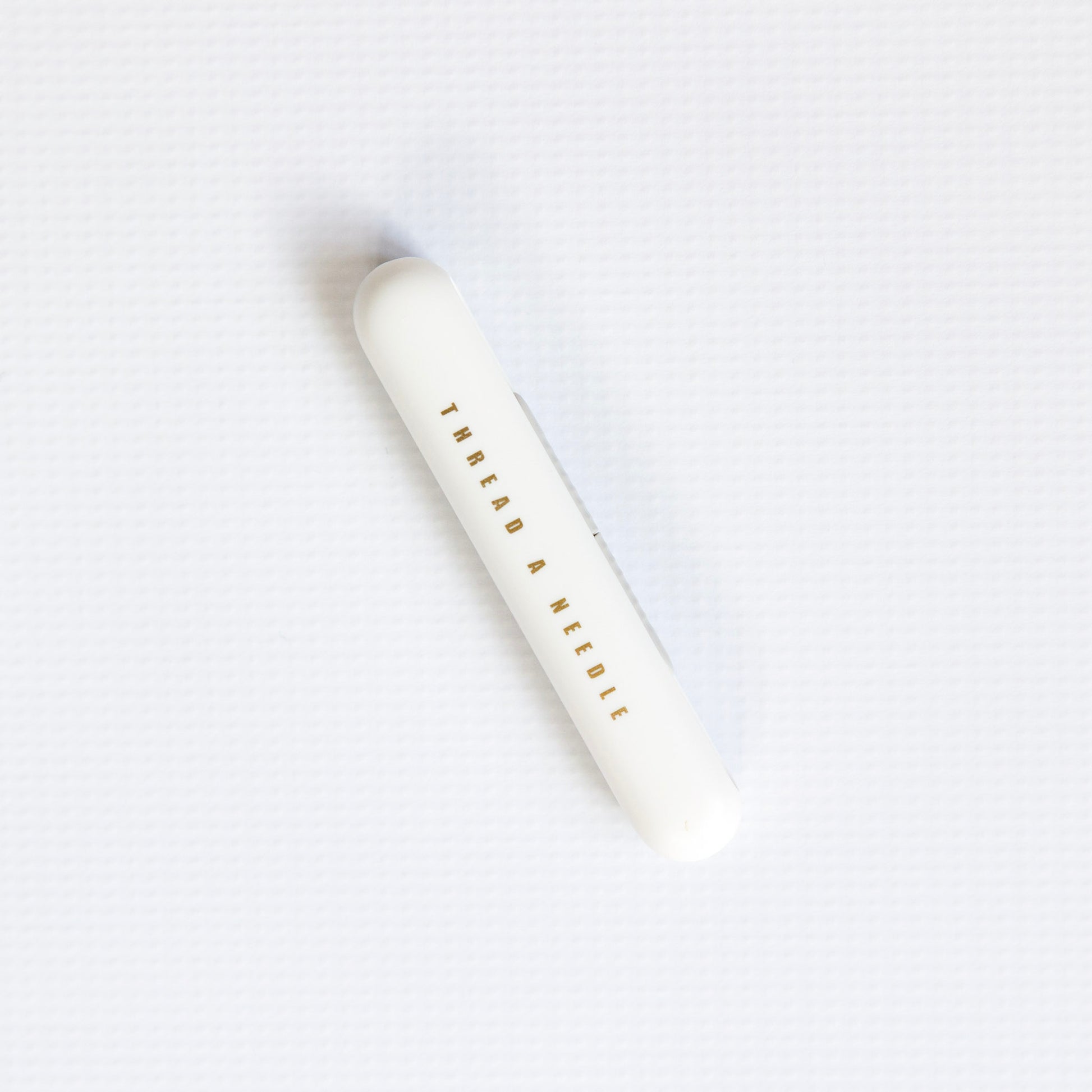 White cylindrical container with 'Thread a Needle' text on a white background