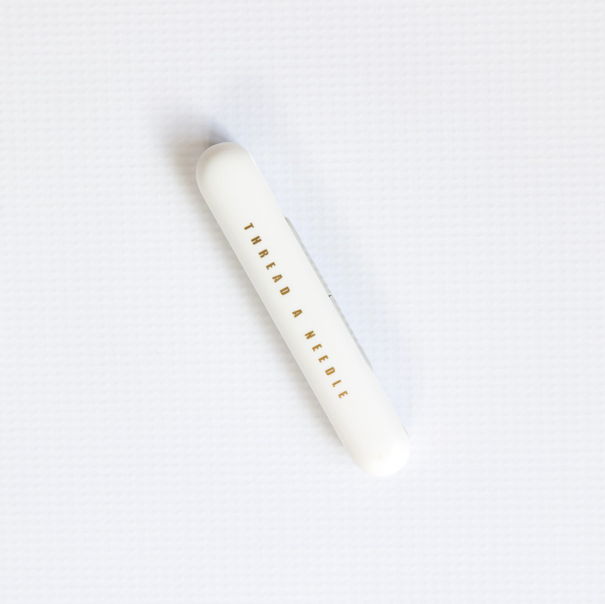 White cylindrical container with 'Thread a Needle' text on a white background