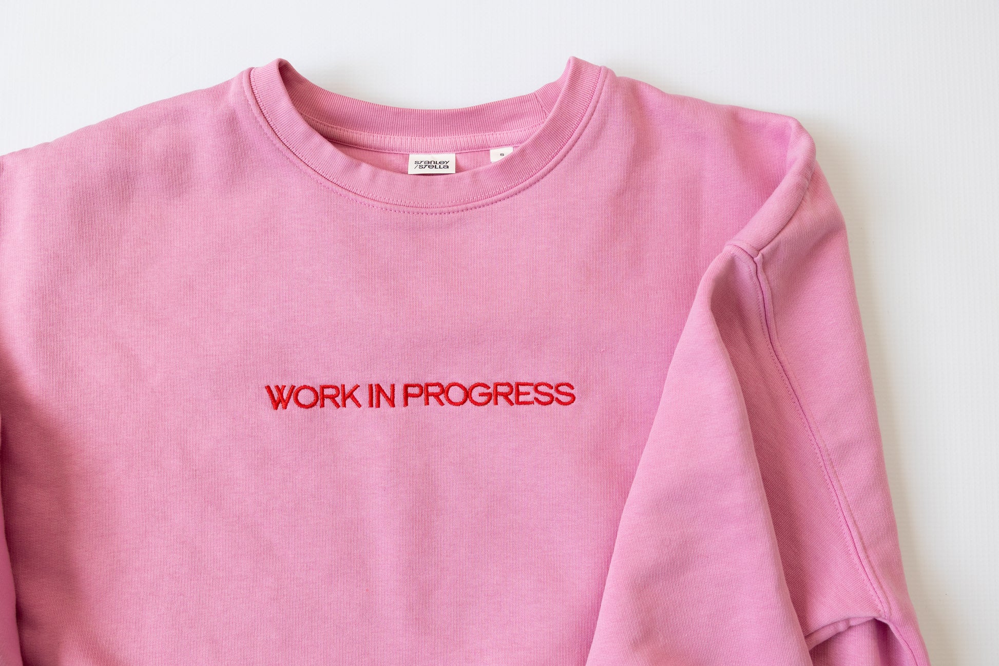 Pink sweatshirt with 'WORK IN PROGRESS' text on a white background