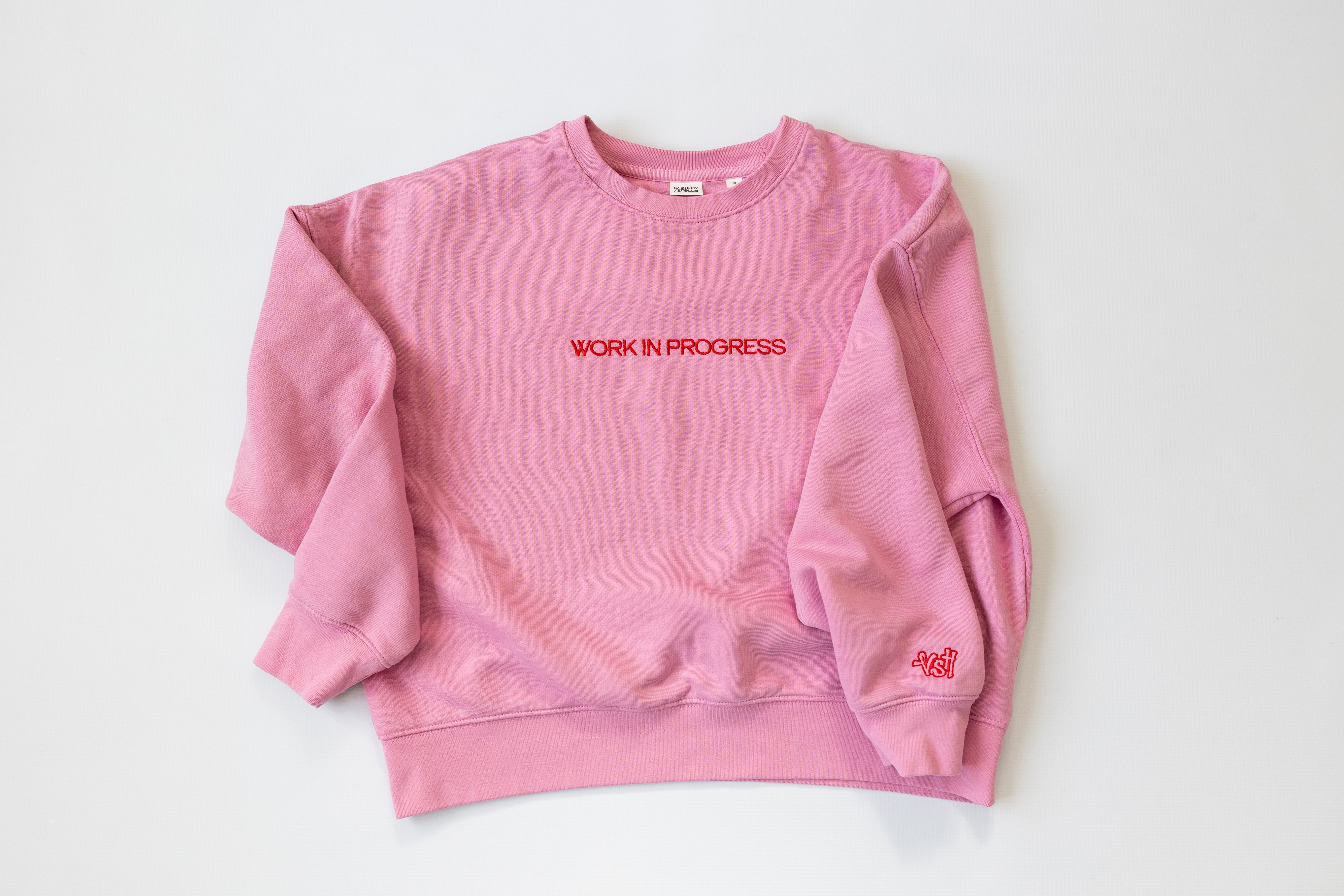 Pink sweatshirt with 'WORK IN PROGRESS' text