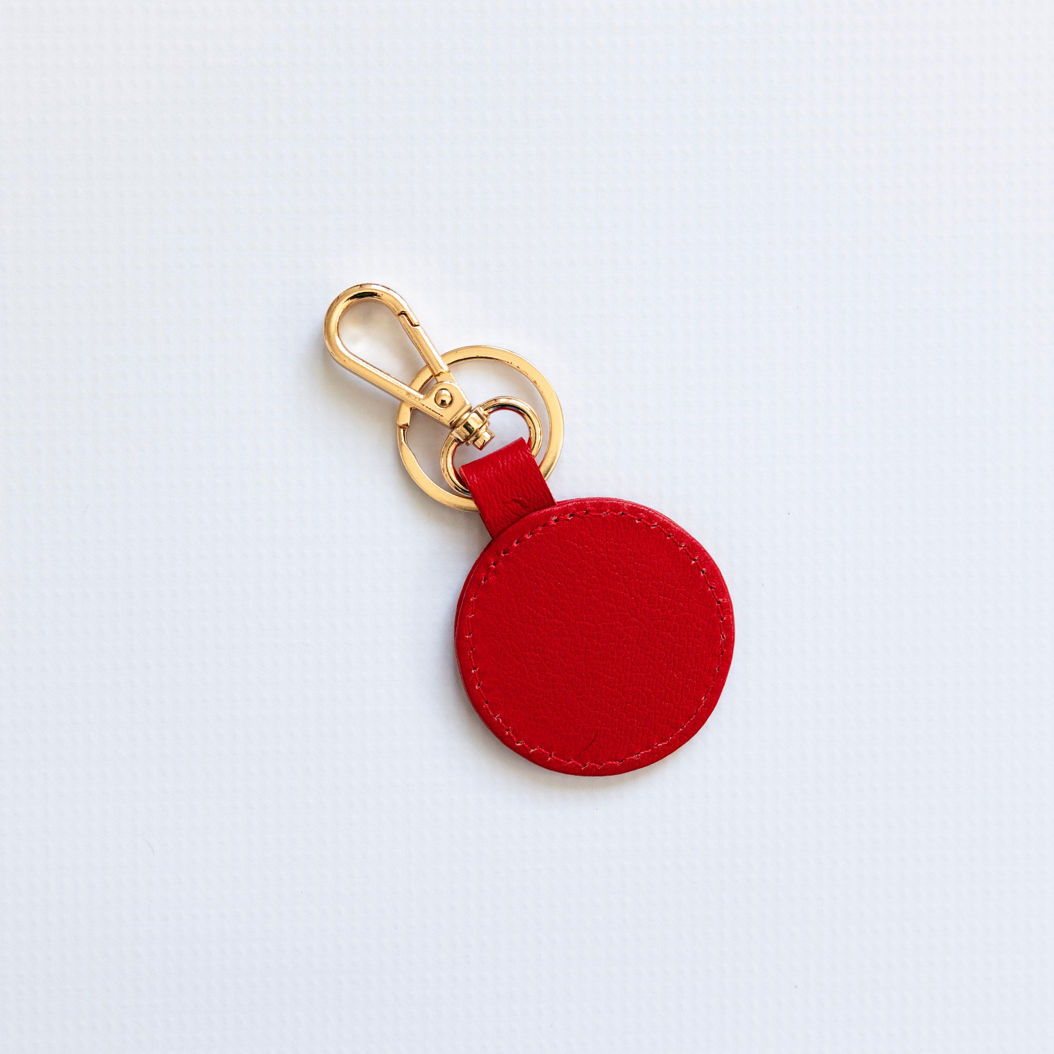 Red round keychain with gold clasp on a light gray background