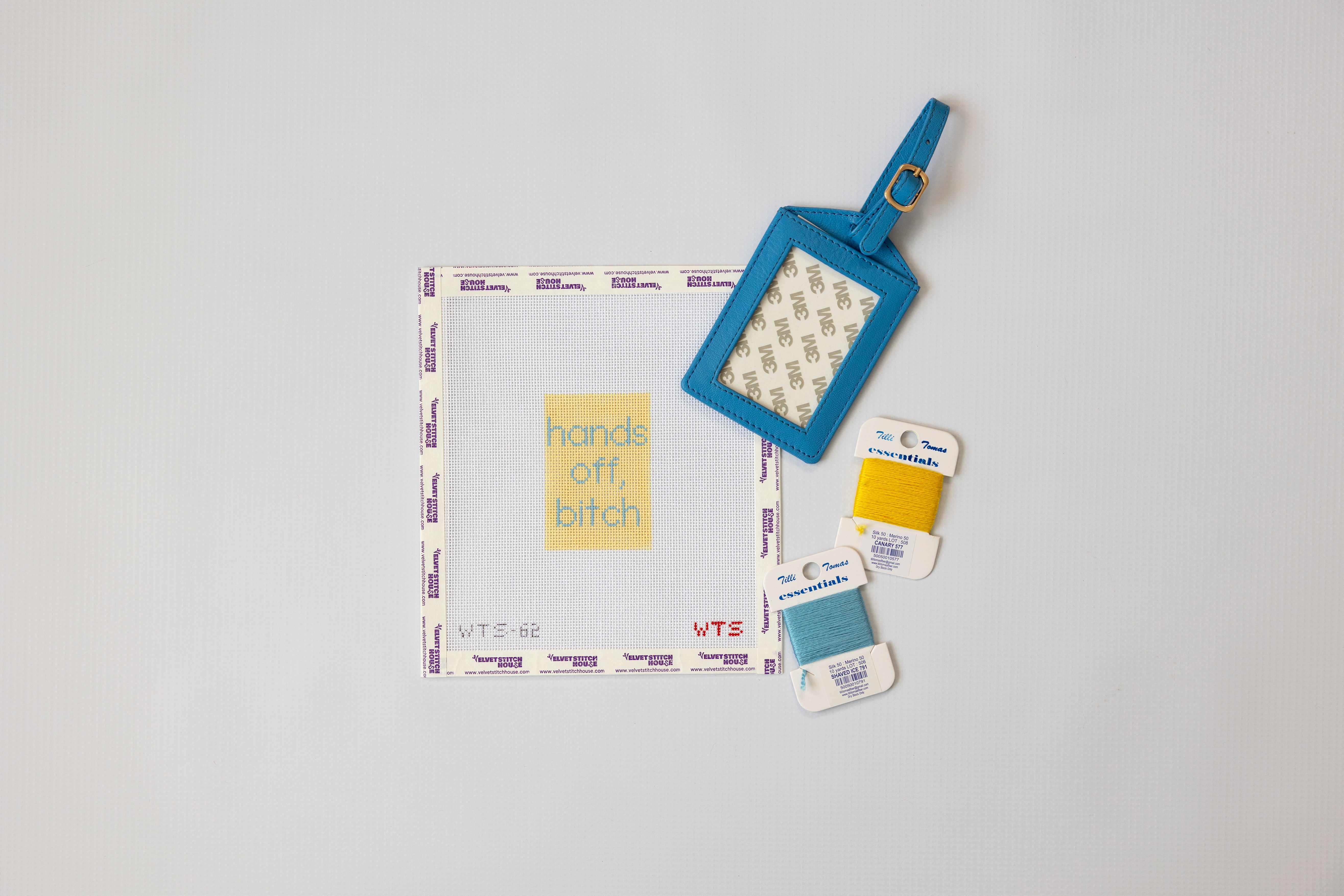 Hands off, bitch luggage tag canvas in yellow background with blue text shown with a blue luggage tag and matching thread.